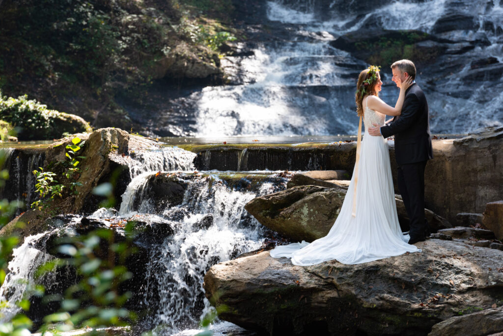Bride and groom stand at the base of a waterfall