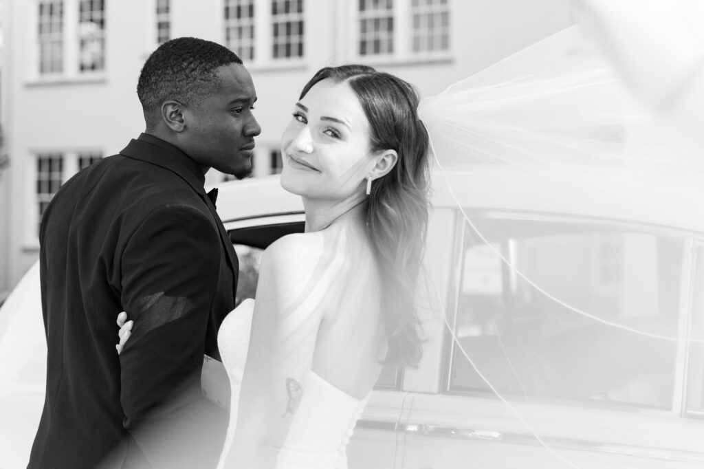 Black groom gazes at his white bride as her veil flies toward the camera