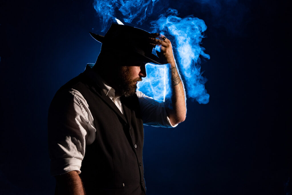 Groom adjusts his hat while blue smoke rises behind him