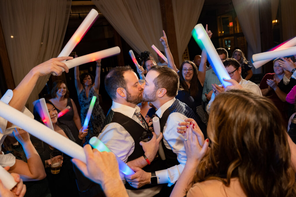 Grooms kiss in the middle of the dance floor with their guests surround them